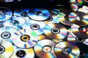 A collection of CDs and DVDs, laid on top of one another in a staggered fashion.