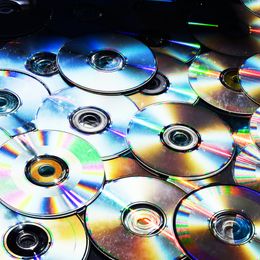 A collection of CDs and DVDs, laid on top of one another in a staggered fashion.