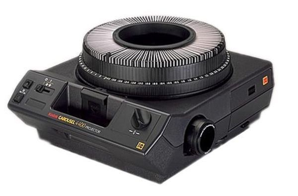 A black and grey Kodak projector with a carousel filled with slides placed on top.