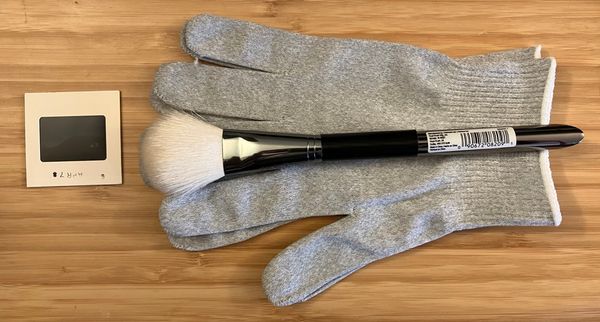 A 35mm slide on the left, a soft paint brush placed on top of nitrile gloves on the right, on top of a wood desk